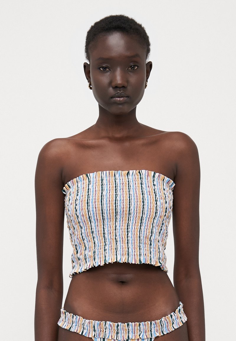 Ermeløs cropped topp med vertikale, flerfargede striper, med smocket tekstur og volangkant. Kombinert med matchende bikini-bukser.