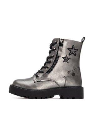 Botas tobilleras metálicas de color plateado con estrellas negras, cierre de cordones en la parte delantera y cremallera en el lateral. Cuentan con una suela gruesa negra y material texturizado.