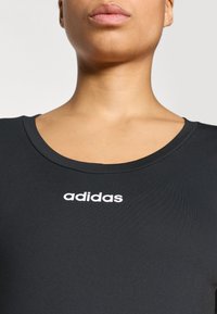 Μαύρο αθλητικό τοπ με στρογγυλή λαιμόκοψη και κοντά μανίκια, με λευκό λογότυπο «adidas» στο στήθος. Λεία υφή.