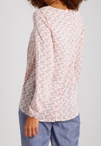 Blusa floreale rosa chiaro, con maniche lunghe, scollatura arrotondata e dettaglio dei bottoni sul retro, realizzata in tessuto leggero.