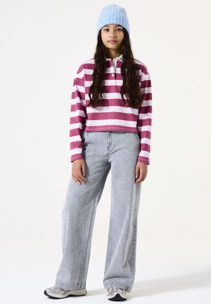 Gestreepte cropped polo in bordeauxrood, roze en wit, gecombineerd met lichtgrijze wijde jeans. Een blauwe gebreide beanie maakt de outfit af.