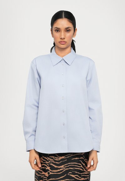 Lyseblå button-up skjorte med spidse kraver, lange ærmer og en glat tekstur, parret med en sort og tan stribet nederdel.