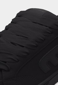 Κοντινό πλάνο μαύρου αθλητικού παπουτσιού με χοντρές υφασμάτινες κορδόνια και ραμμένο λογότυπο στην πλευρά.