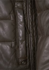 Dunkelbraune Lederjacke mit gestepptem Design, seitlichem Reißverschluss und Druckknopfakzenten an der Taschenklappe sowie der Schulternaht.