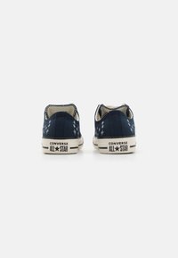 Baskets basses en toile bleue avec un motif étoile blanc, semelle en caoutchouc et logo noir "CONVERSE ALL STAR" sur le talon.