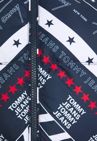 Granatowa pikowana kurtka z zapięciem na zamek. Posiada wzory białych i czerwonych gwiazd oraz logo marki na całej powierzchni. Gładka, błyszcząca tekstura.