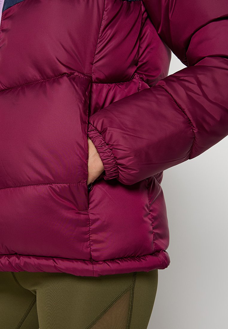 Chaqueta de plumas color marrón con diseño acolchado, puños elásticos y bolsillos laterales. Hecha de un material suave y brillante con una silueta redondeada.