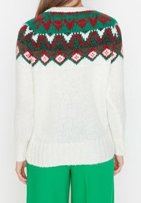 Weißer Strickpullover mit einer grün, rot und weiß gemusterten Passe, die Herzen und Rauten zeigt; gerippter Saum und Bündchen.