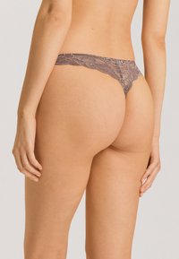 Kanten stringt met een delicate bloemenpatroon, met een zachte, muted grijze kleur en gegolfde randen, ontworpen voor minimale bedekking.