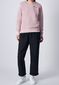 Felpa rosa in cotone con colletto rotondo e logo ricamato. Abbinata a pantaloni neri larghi e sneakers bianche.