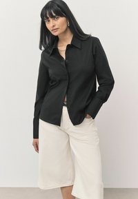 Zwarte button-up shirt met een kraag, lange mouwen en een gladde textuur, gecombineerd met crèmekleurige brede broekspijpen. Eenvoudig en tailleren ontwerp.