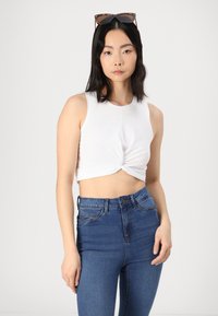 White sleeveless crop top with a knotted front, paired with high-waisted blue denim jeans featuring front pockets and a button closure.