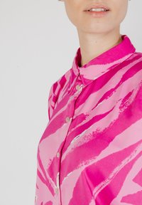 Blusa rosa con cuello, que presenta un patrón de rayas diagonales en tonos más claros y más oscuros de rosa, y con detalles sutiles de botones.
