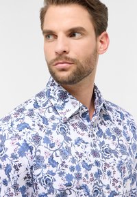 Witte shirt met een blauw bloemenpatroon met ingewikkelde details en variërende tinten, aangevuld met een standaard kraag en een zachte textuur.