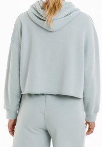 Lichtblauwe cropped hoodie gemaakt van zachte stof, met een grote capuchon, verlaagde schouders en een ruwe zoomafwerking.