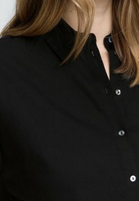 Camicia nera con colletto, dotata di una pattina e bottoni neri lucidi; il tessuto appare liscio e leggero.