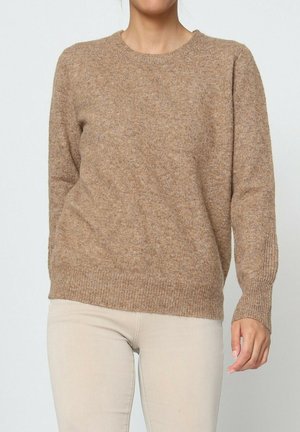 Pull en tricot marron avec un col rond, des poignets et un ourlet côtelés. Texture douce et coupe décontractée, porté sur un pantalon beige clair.