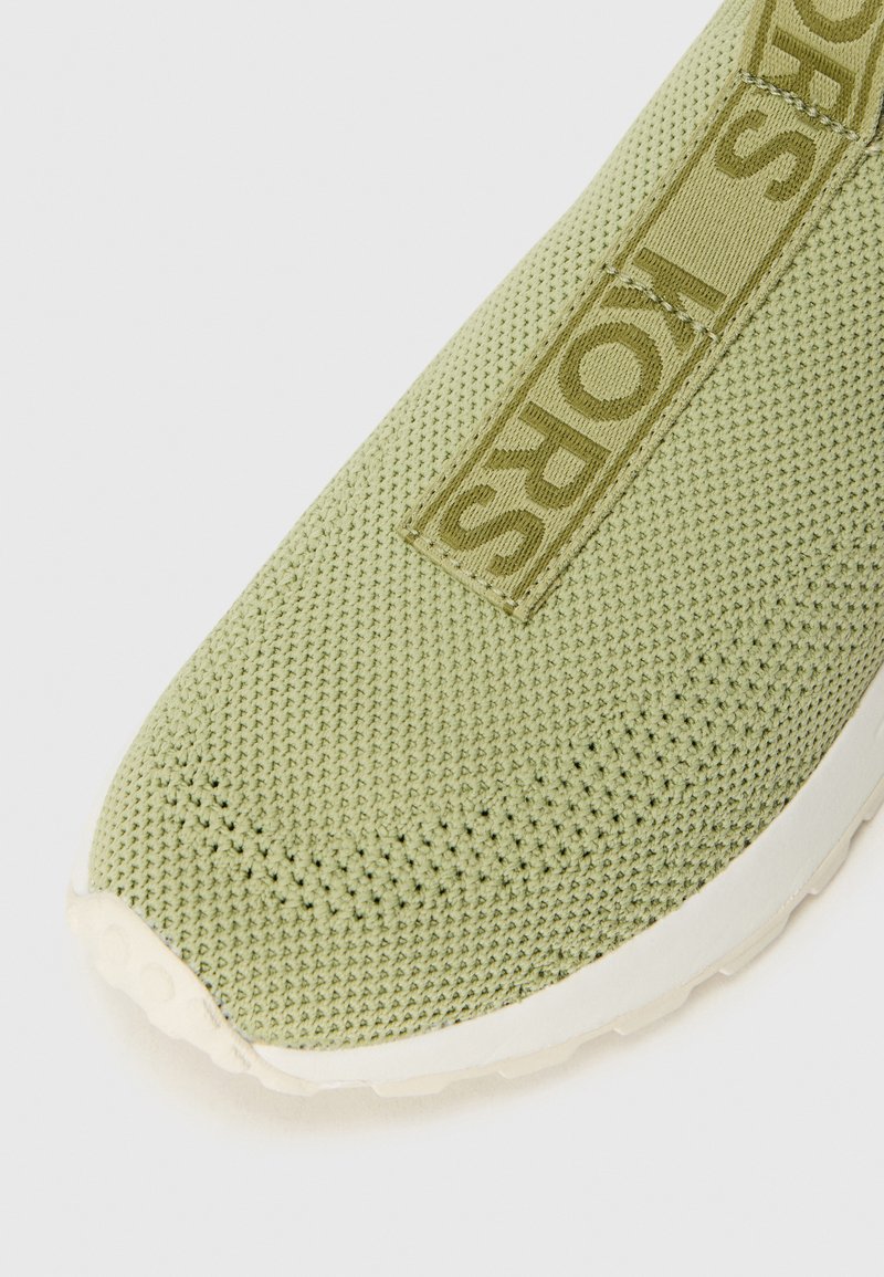 Gros plan sur une tige de sneaker vert clair présentant un design en maille texturée et une étiquette de logo de marque bien visible sur le côté.