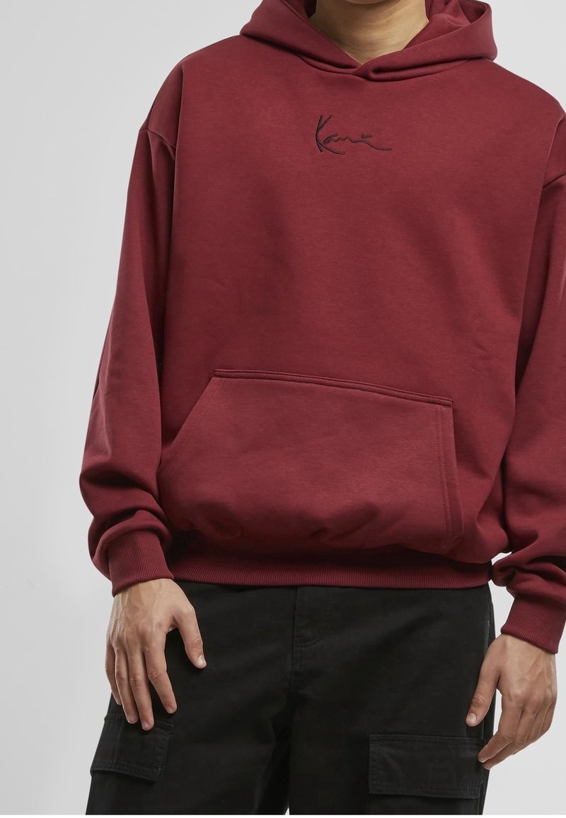 Sweat à capuche en coton bordeaux avec poche kangourou à l'avant, poignets et ourlet côtelés. Présente un logo brodé en noir au-dessus de la poche.