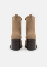 Beige suede ankle boots with a rounded toe, side zippers, and a ribbed brown block heel. Smooth texture and simple vertical seam design.