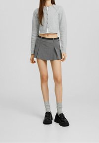 Cardigan grigio corto, top aderente nero, gonna corta grigia a pieghe e scarpe nere chunky. Maglia testurizzata, tessuti lisci e calze sovrapposte.