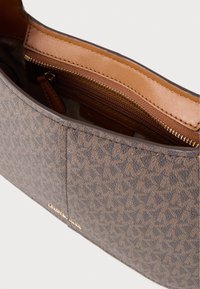 Καφέ τσάντα χειρός με σχέδιο και κύριο διαμέρισμα με φερμουάρ, επένδυση από λείο δέρμα σε ανοιχτή καφέ απόχρωση. Διαθέτει διακοσμητικά σε χρυσό τόνο.