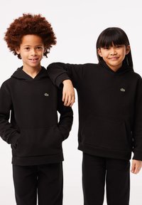Felpe con cappuccio nere realizzate in morbido tessuto, dotate di una tasca frontale e di un piccolo logo verde, indossate da due bambini.