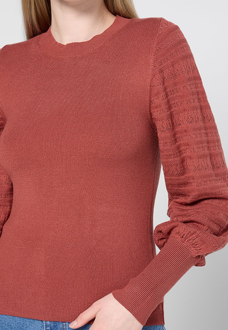 Pull rouge côtelé avec des manches bouffantes texturées et un col rond. Fabriqué dans un matériau doux, avec un corps lisse et des poignets élastiques.