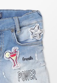 Pantalones cortos de mezclilla azul claro con bordes deshilachados, que cuentan con un parche de estrella de lentejuelas, un cóctel bordado y texto impreso "fresco" y "PODER".