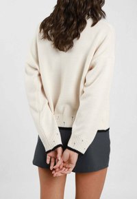 Maglione in maglia color crema con vestibilità rilassata, caratterizzato da orlo e polsini a coste neri; la parte posteriore mostra una trama sottile e maniche ampie.