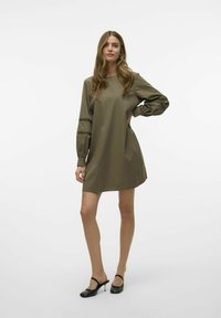 Olijfgroene jurk met lange, opgezette mouwen met uitsnijdingen. Eenvoudige A-lijnvorm, gemaakt van gladde stof. Gekocht met zwarte hakken.