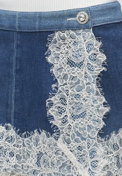 Τζιν φούστα με λευκή δαντελένια επικάλυψη με floral μοτίβο και ένα κουμπί με στρας στη μέση, σε συνδυασμό με ένα λευκό ριμπ μπλουζάκι.
