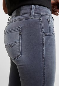 Grå denimjeans med en figurnära design, som har en distinkt form på bakfickorna, stickningsdetaljer och en läderlogotyp på midjan.