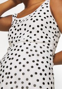 Harmaa ilmanhihaista mekkoa, jossa on mustia pilkkuja, pehmeä rakenne ja tiukka muotoilu. Kangas on sileä ja kevyt.