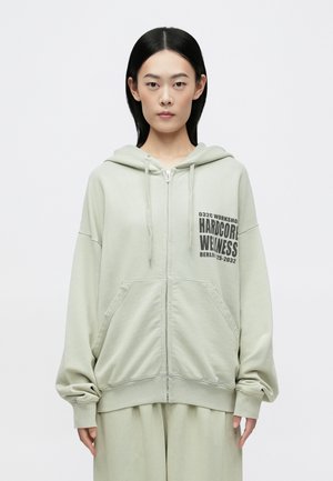 Világoszöld, cipzáras kapucnis pulóver, elöl logónyomattal, laza fazonnal és két elülső zsebbel. Puha anyagból készült, bordázott mandzsettákkal.