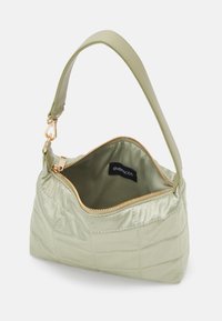 Sac à main matelassé vert clair avec une fermeture éclair dorée partiellement ouverte, une seule sangle courte et une étiquette de marque noire à l'intérieur.