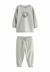 Harmaa puuvillatrikoo-sweatshirt, jossa on musta hymyilevä naama -grafiikka, yhdistettynä samanvärisiin harmaisiin sweats-housuihin, joissa on joustava vyötärö ja hihansuut.