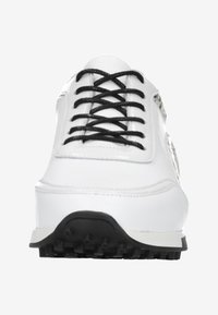 Białe trampki z czarnymi sznurowadłami, gładka syntetyczna cholewka oraz teksturowana czarna gumowa podeszwa z małymi wypustkami zapewniającymi przyczepność.