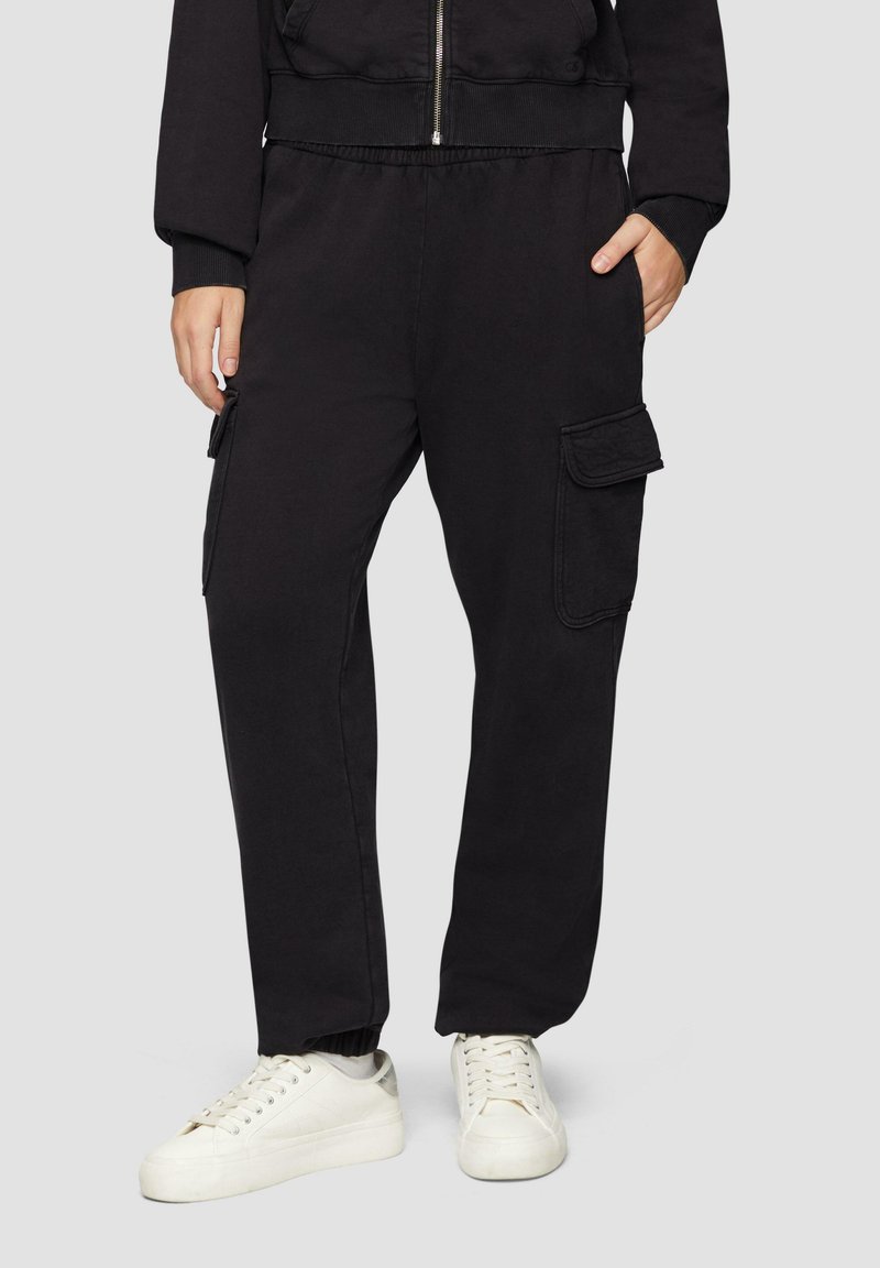 Pantalones cargo negros hechos de tela suave, con bolsillos laterales, una cintura elástica y un corte holgado. Combinados con zapatillas blancas.