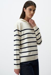 Cremefarbener Hoodie mit marineblauen Streifen, weicher Textur, lockerer Passform, gerippte Bündchen und Saum, ausgestattet mit einer Vordertasche und verstellbarem Kordelzug an der Kapuze.
