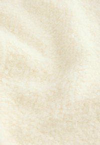 Tissu doux de couleur crème avec une surface texturée, bouclée et légèrement frisée, laissant apparaître des plis et des ombres subtils.