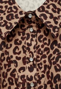 Gros plan d'une chemise à imprimé léopard avec un col pointu et quatre boutons-pression ronds argentés sur le devant.