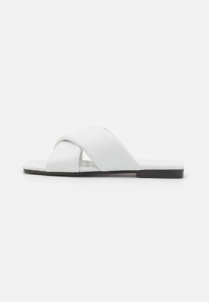 Witte leren slidesandalen met een kruislings ontwerp, platte zool en open teen. Gladde textuur en minimalistische stijl met een zwarte zool.