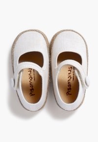 White canvas Mary Jane shoes with round toe, tan textile lining, and a decorative strap with a button. Textured sole edges.