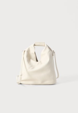 Crème kleurige leren tas met een uniek gaatjesdesign aan de bovenkant, verstelbare schouderriem en een gladde textuur. Eenvoudige, minimalistische vorm.