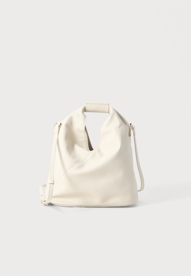 Bolsa de couro em cor creme com um design único de buracos na parte superior, alça ajustável e textura suave. Forma simples e minimalista.