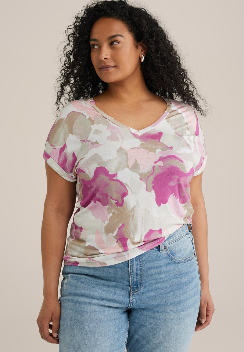 V-neck gėlių marškinėliai su rožine, smėline ir balta abstrakčia_pattern, minkšta medžiaga, trumpomis rankovėmis su apvadu, derinami su mėlynomis džinsinėmis kelnėmis.