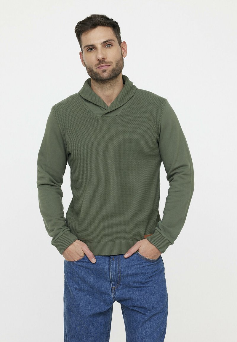 Grüner Pullover aus strukturiertem Material mit Schalkragen, gerippten Manschetten und Saum, kombiniert mit blauen Jeans, steht vor einem neutralen Hintergrund.