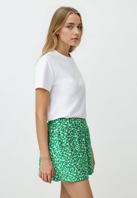 T-shirt bianco a maniche corte abbinato a una gonna verde con motivo floreale. La gonna presenta un design svasato con motivi floreali bianchi.