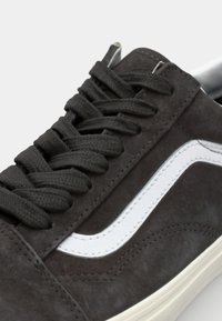 Svart semsket sneakers med hvit side stripe, runde snørebånd og strukturert overdel. Har sømdetaljer og en kremfarget gummisåle.